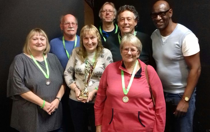 6 people pictured wearing medals and holding a trophy for winning the quiz.