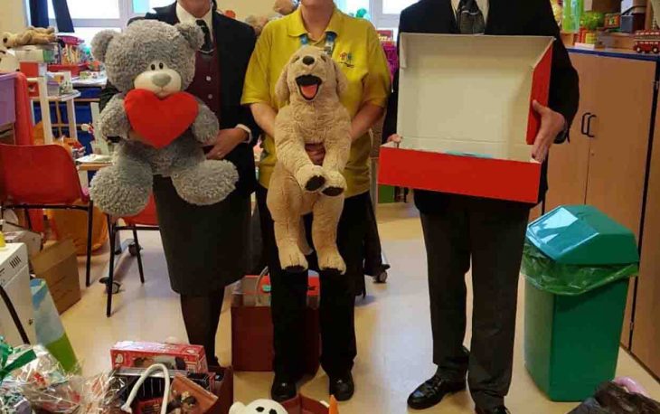 3 colleagues from Bexley standing each holding a grey teddy, a stuffed dog and a red open box.