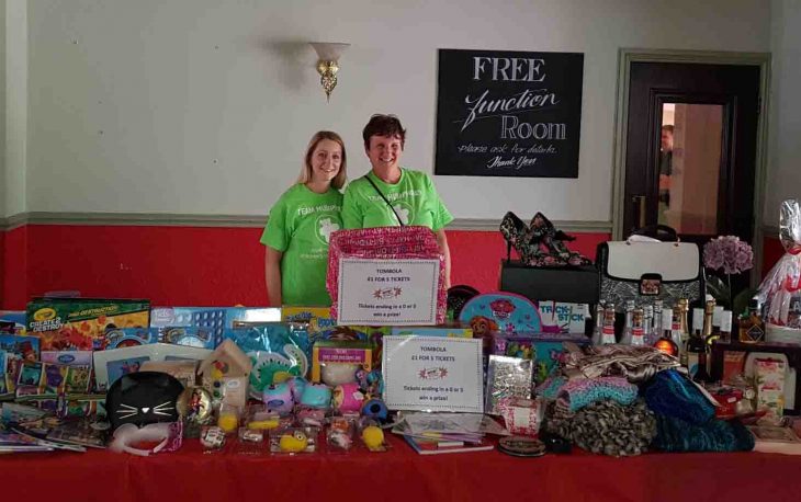 Two women standing next to a table with various items.