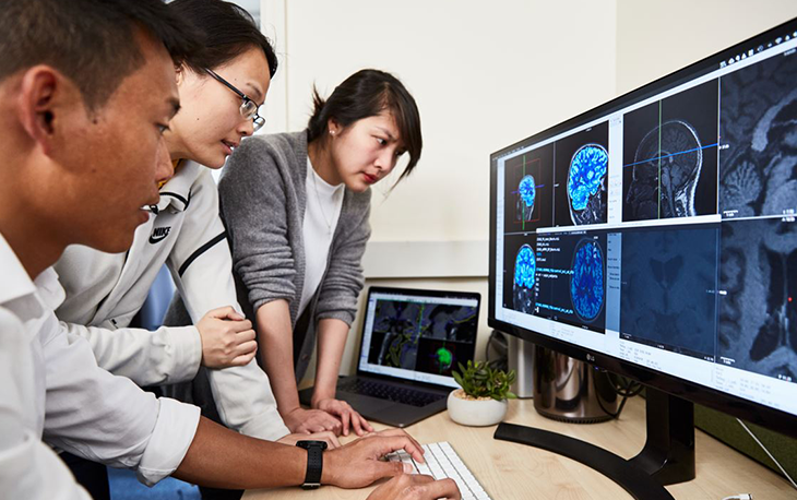 Picture of 3 doctors looking at computer screens with images of brain scans.