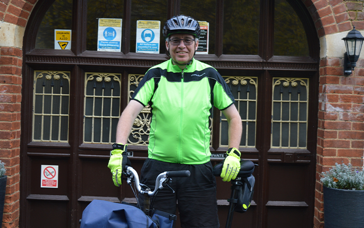 A man wearing a helmet and lime green gloves standing with his bicycle.