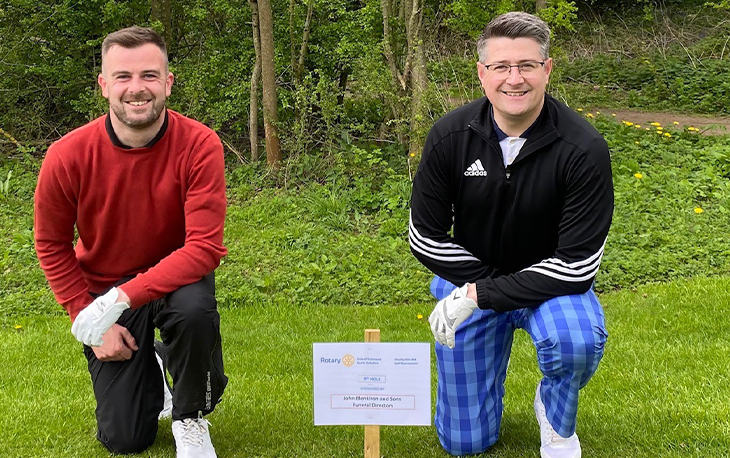 Two men dressed in Gold attire kneeling on the grass next to sign with their names.