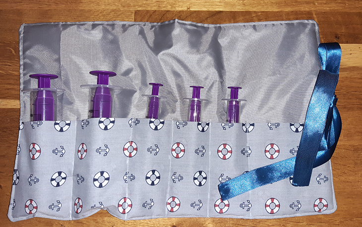 Picture of a blue patterned square with slots to put syringes for children, which can be tied up with the blue ribbon.