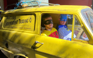 Two men dressed as Batman and Robin inside bright yellow car 'Totters Independent Trading Co'