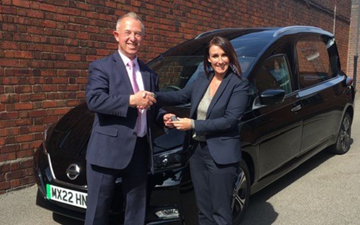 Two employees from William H Painter Funeral Directors shaking shaking hands and holding keys to a new eco hearse.