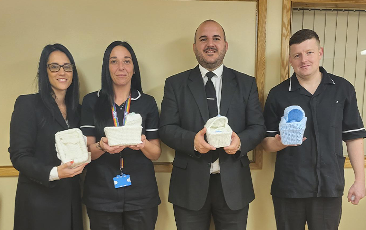 Workers from W Storey Funeral Services holding tiny knitted cribs that were donated.