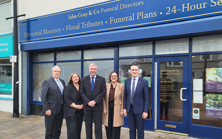 4 people standing in front of dark blue John Gray & Co Funeral Directors branch.