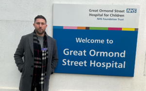 A man standing in front of a sign for Great Ormond Street Hospital.